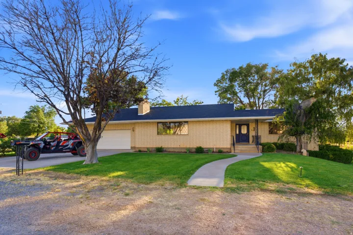 Ranch-style exterior featuring a light brick facade, dark roofing, and an integrated garage
