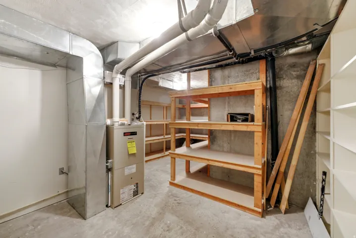 Utility area with concrete flooring, exposed ductwork, built-in shelving, and a forced-air furnace