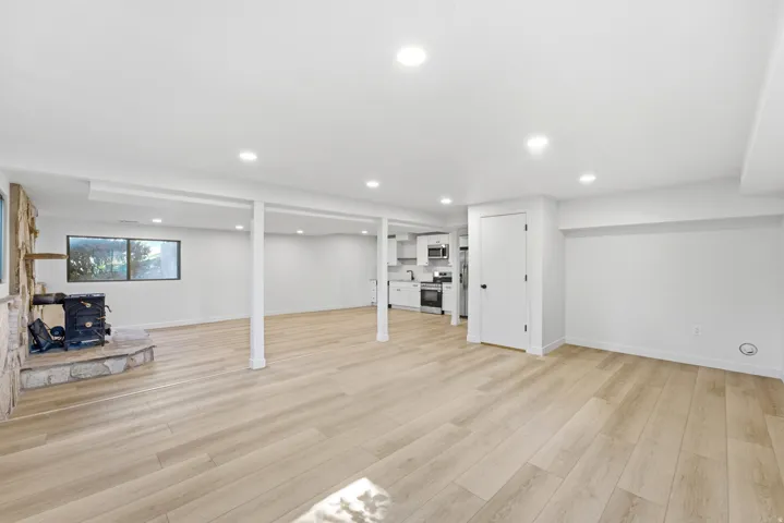 Spacious lower-level area featuring wood-finish flooring, recessed lighting, and a stone-clad fireplace with a wood stove insert