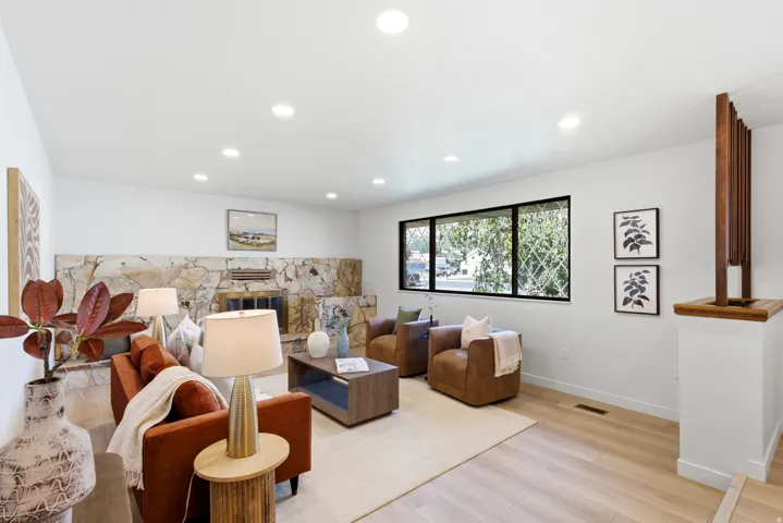 Living space featuring a stone fireplace with hearth, light wood-finish flooring, recessed lighting, and large windows with black frames