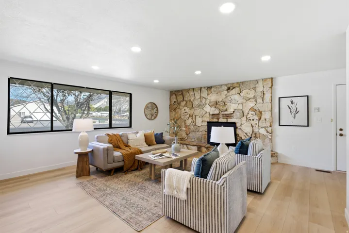 Living area featuring a floor-to-ceiling stone fireplace, recessed lighting, expansive windows with black frames, and light wood-finish flooring