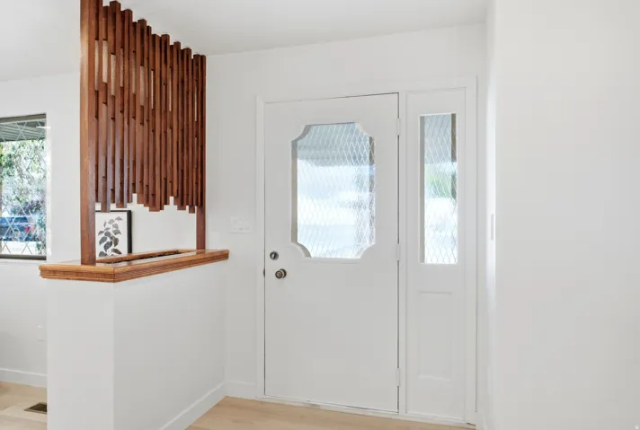Entryway featuring a white door with decorative glass inserts, a coordinating sidelight, a vertical wood slat room divider, and light wood-finish flooring