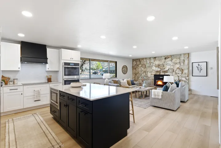 Open-concept living space featuring wood-finish flooring, a stone-clad fireplace, and recessed lighting