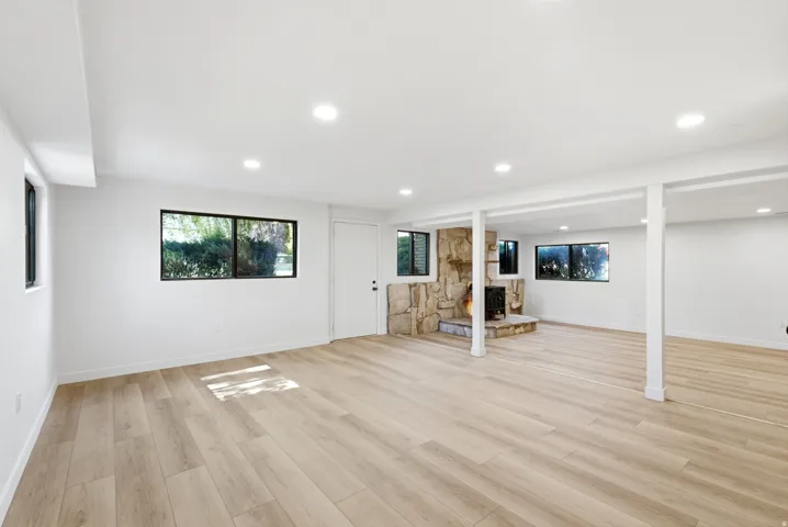 Spacious room featuring light wood-finish flooring, recessed lighting, and a stone-faced fireplace with a hearth