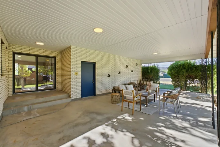 Expansive covered patio featuring a concrete surface, white brick exterior, recessed lighting, and a dark blue entrance door