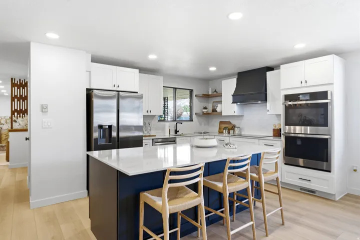 Gourmet kitchen with a large center island featuring a white countertop and seating, stainless steel appliances, white cabinetry, a dark range hood, and light wood-finish flooring