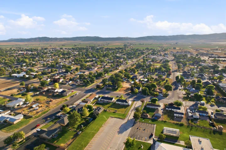 Expansive aerial capturing a suburban landscape with residential streets, mature trees, and open fields under a clear sky