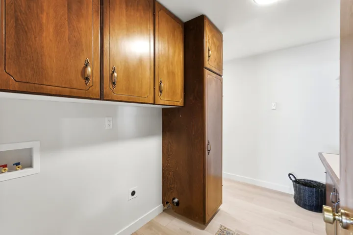 Utility room featuring wood cabinetry with decorative pulls, light wood-finish flooring, and white walls
