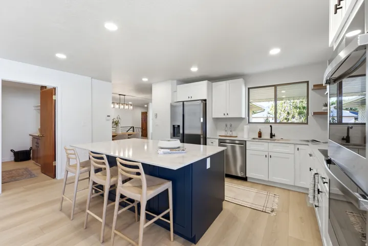 Modern kitchen featuring a large central island with seating, light wood-finish flooring, white upper and lower cabinetry, stainless steel appliances, and recessed lighting