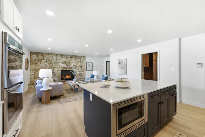 Kitchen island with a light-toned countertop and built-in microwave, complemented by white upper cabinetry and integrated double ovens