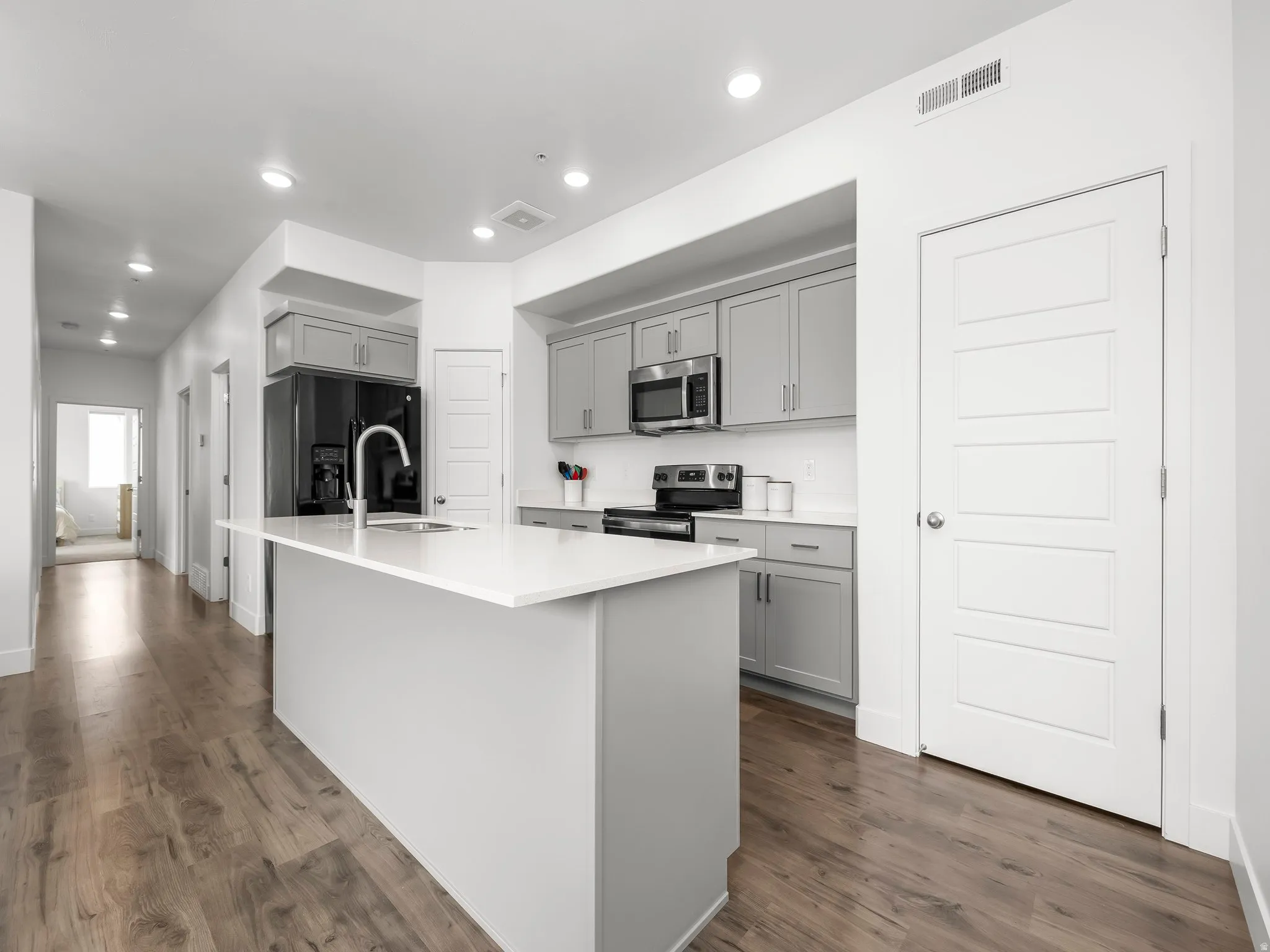 Kitchen featuring gray cabinets, stainless steel appliances, a kitchen island with sink, recessed lighting, and dark wood-style flooring