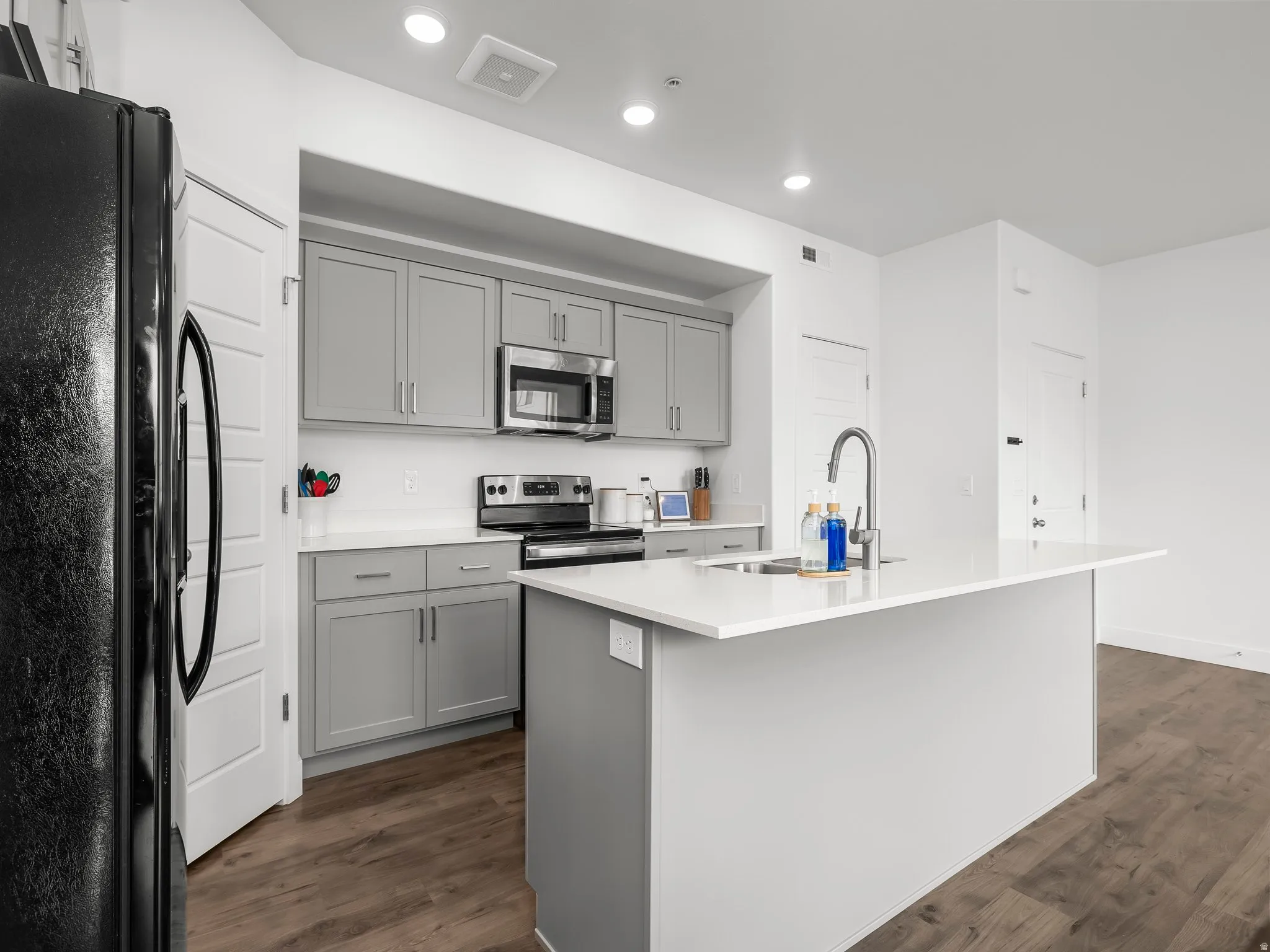 Kitchen with stainless steel appliances, gray cabinets, dark wood-style floors, a kitchen island with sink, and recessed lighting