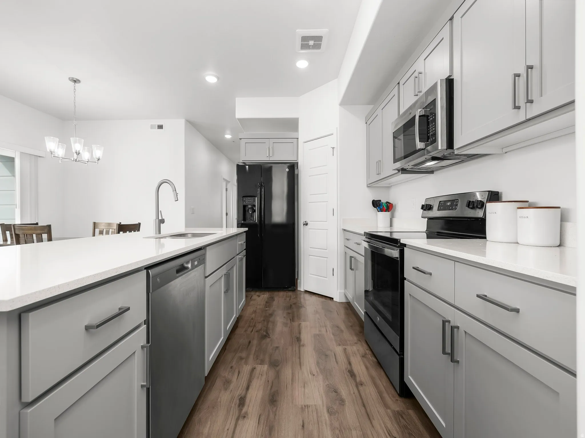 Kitchen with gray cabinets, stainless steel appliances, dark wood-style floors, a center island with sink, and suspended lighting