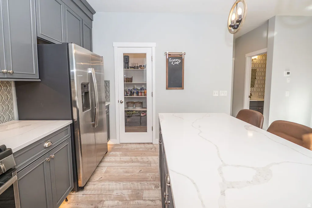 Kitchen featuring gray cabinets, light stone counters, stainless steel appliances, a kitchen bar, and light wood-type flooring