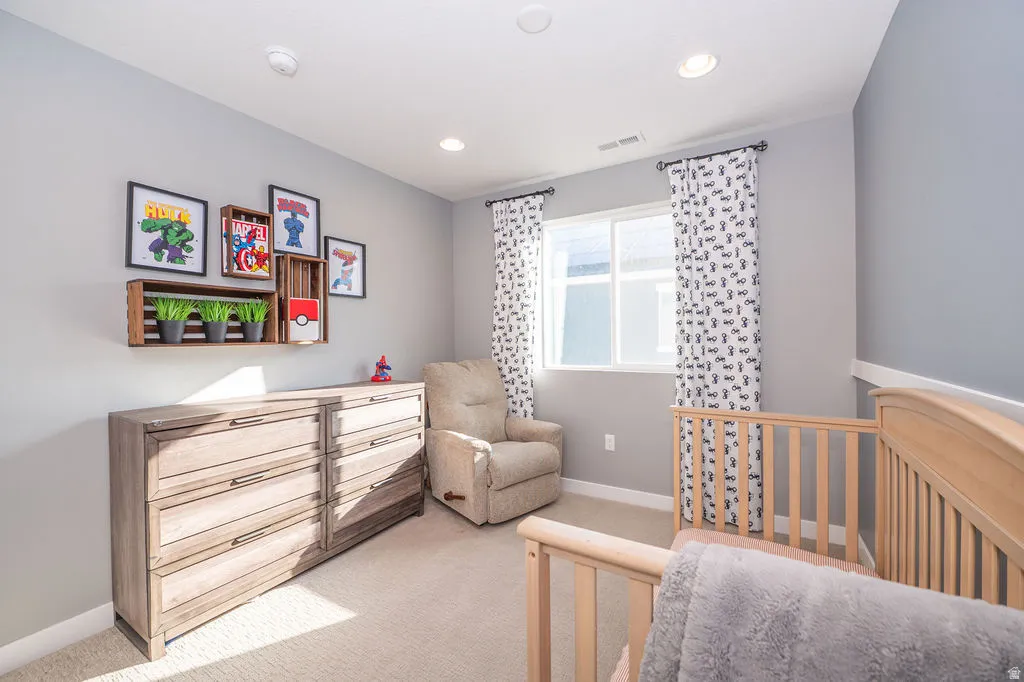 Bedroom featuring light colored carpet, a nursery area, and recessed lighting