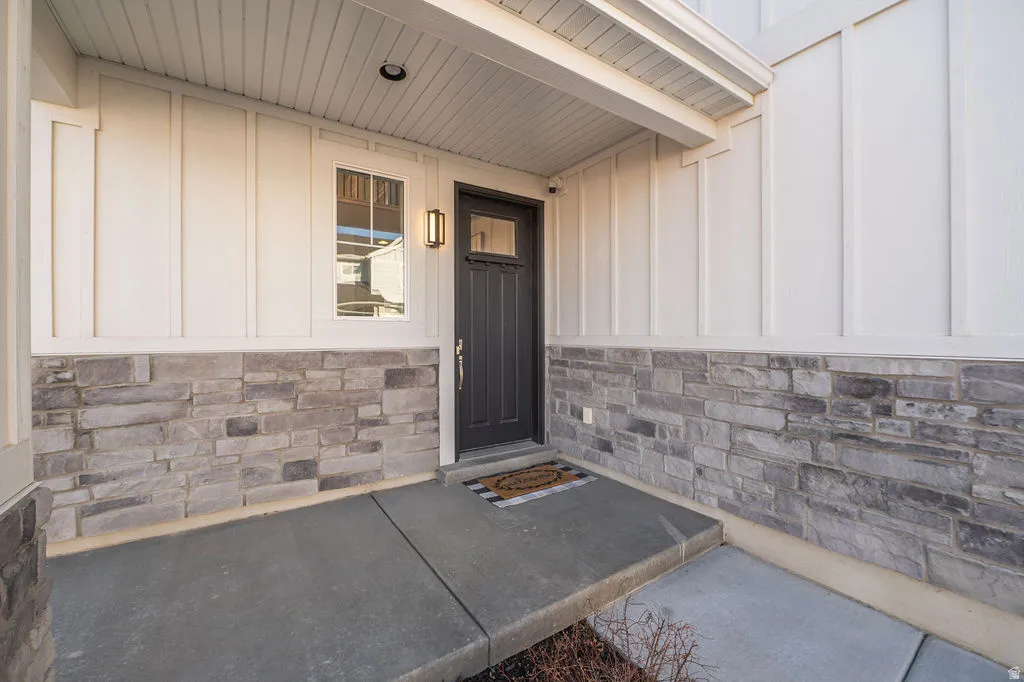 Property entrance with board and batten siding, stone siding, and covered porch