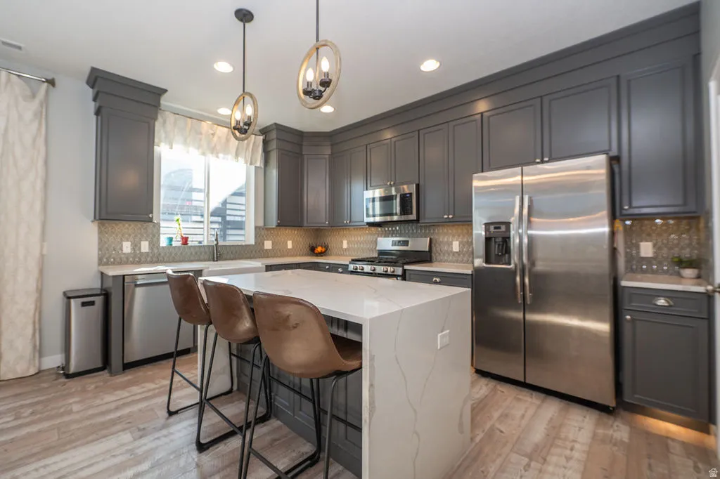 Kitchen with stainless steel appliances, a kitchen breakfast bar, a center island, light stone countertops, and light wood-type flooring