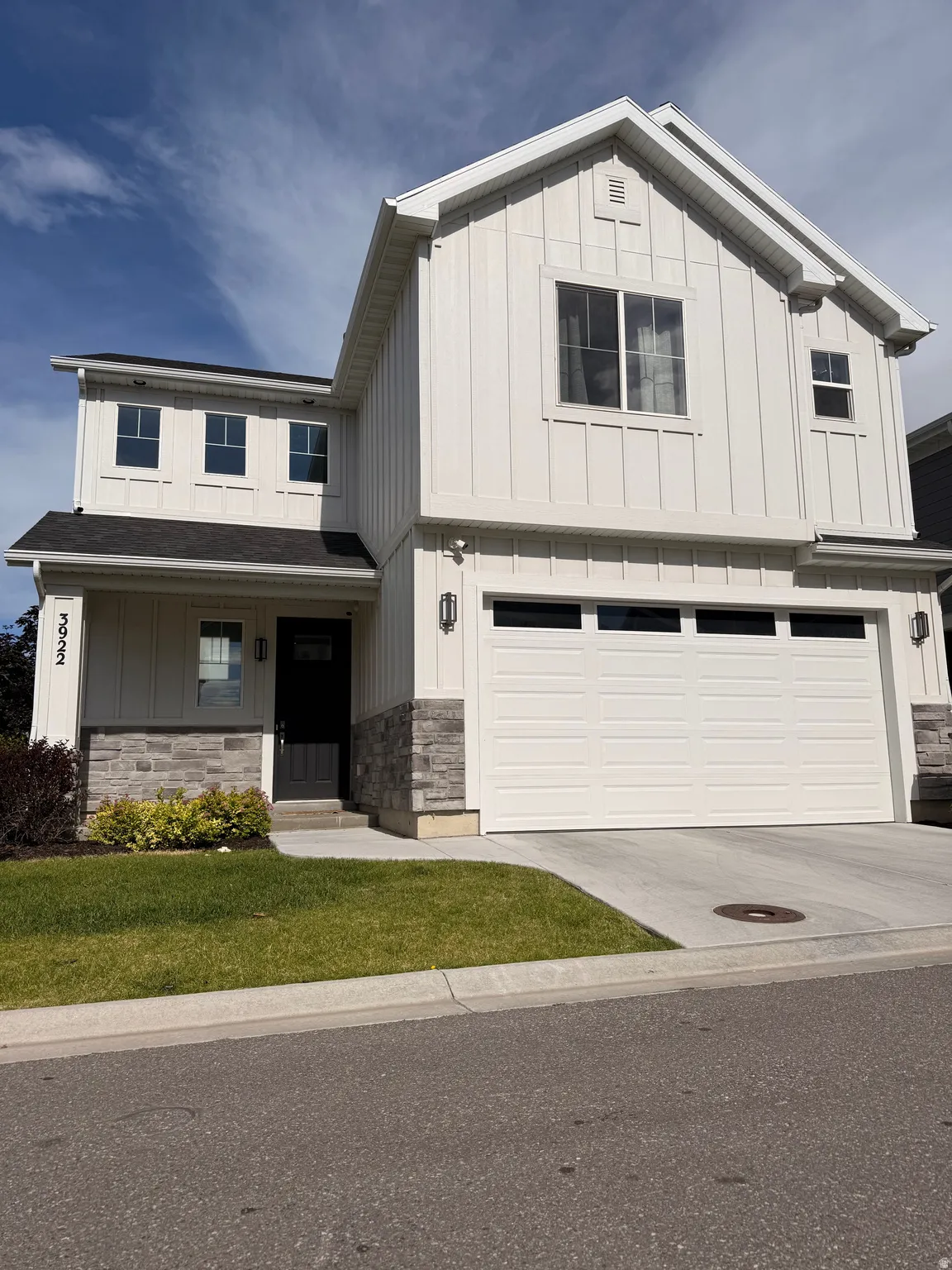 Contemporary two-story residence featuring white board and batten siding, dark stone accent work, an attached two-car garage, and a covered entry