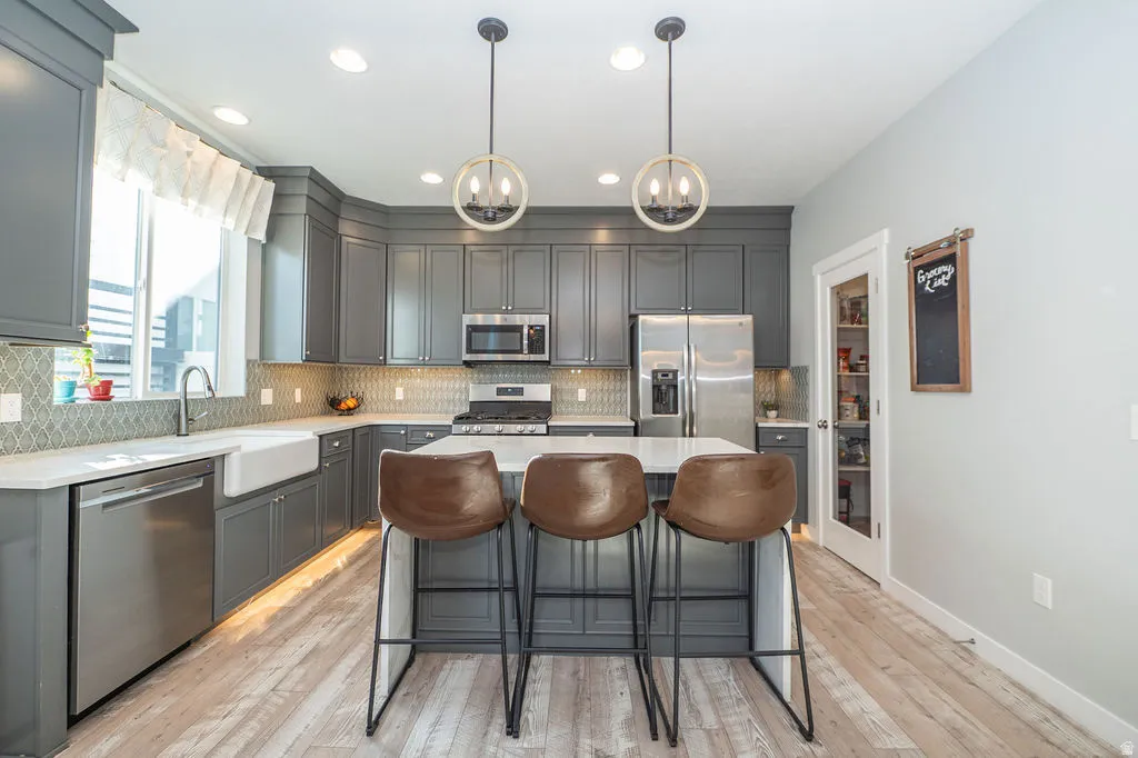 Kitchen featuring gray cabinets, stainless steel appliances, a kitchen bar, decorative backsplash, and a center island