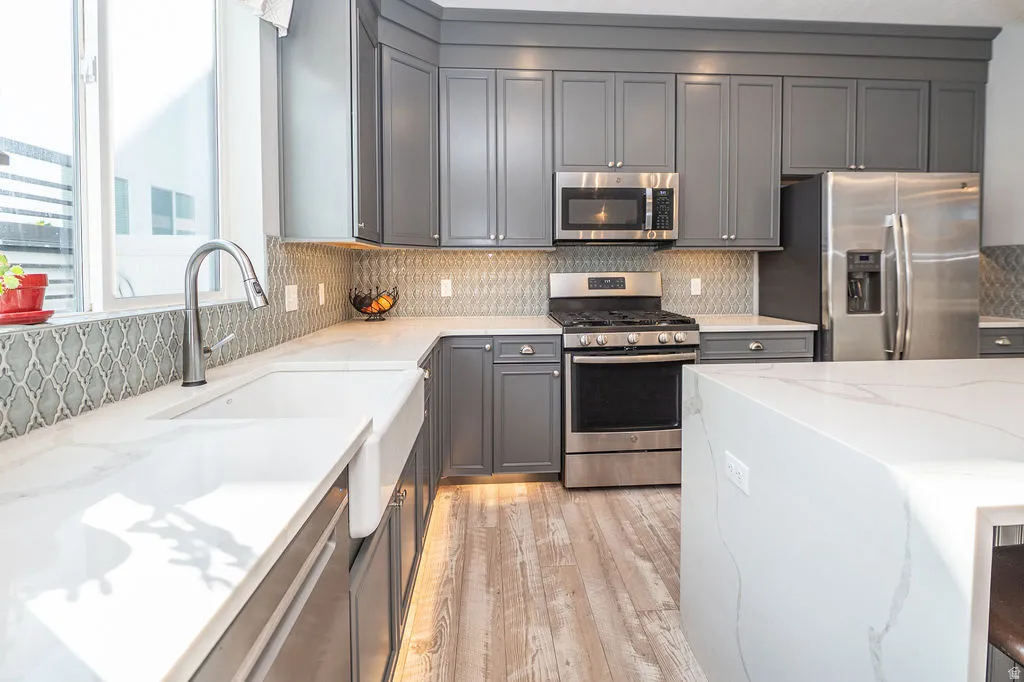 Kitchen featuring gray cabinetry, light stone counters, stainless steel appliances, and backsplash