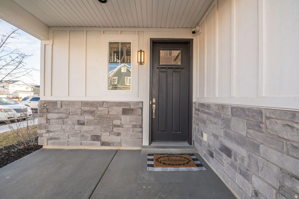 View of exterior entry with stone siding, board and batten siding, and covered porch