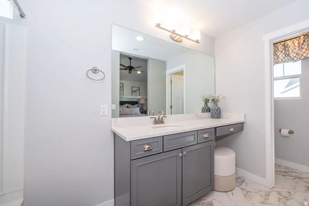 Ensuite bathroom featuring vanity, light marble finish floors, and a ceiling fan