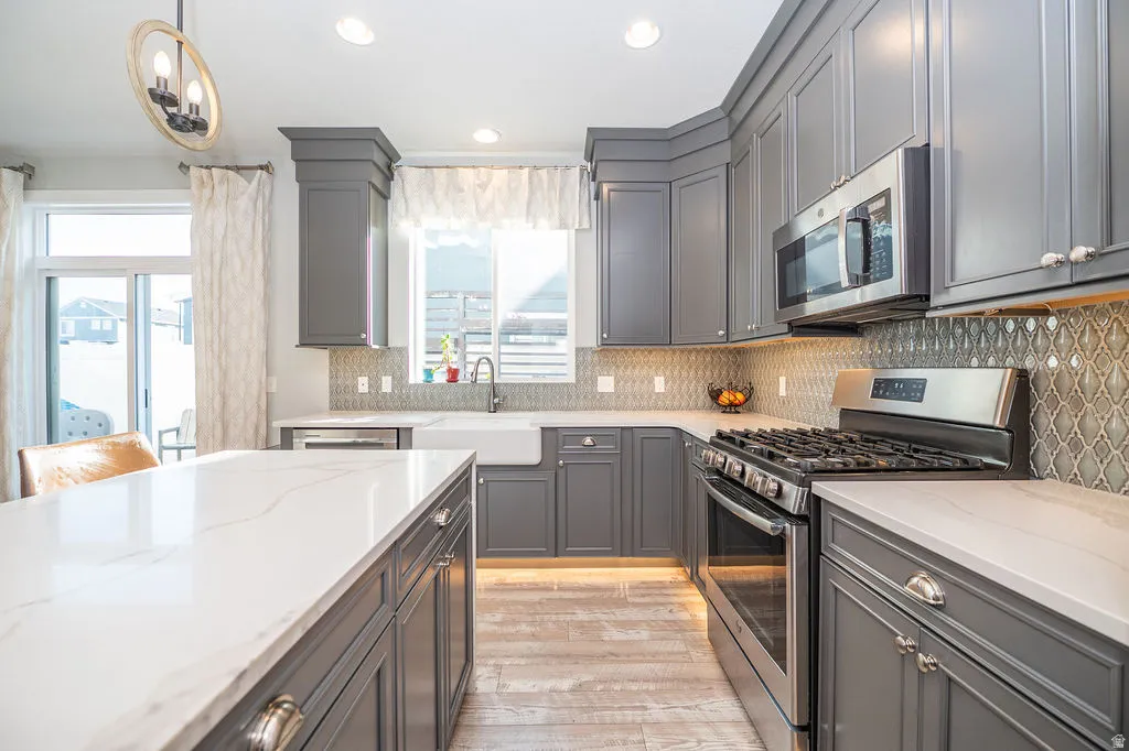 Kitchen with gray cabinetry, stainless steel appliances, light stone counters, and light wood-style flooring