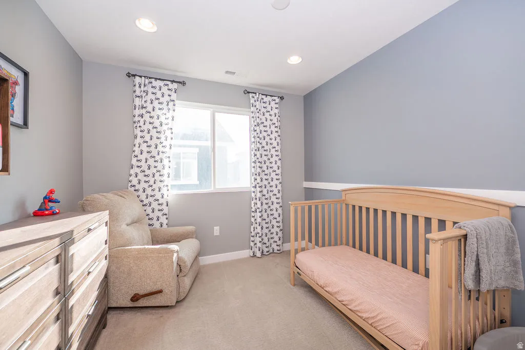 Bedroom with a crib, light colored carpet, and recessed lighting