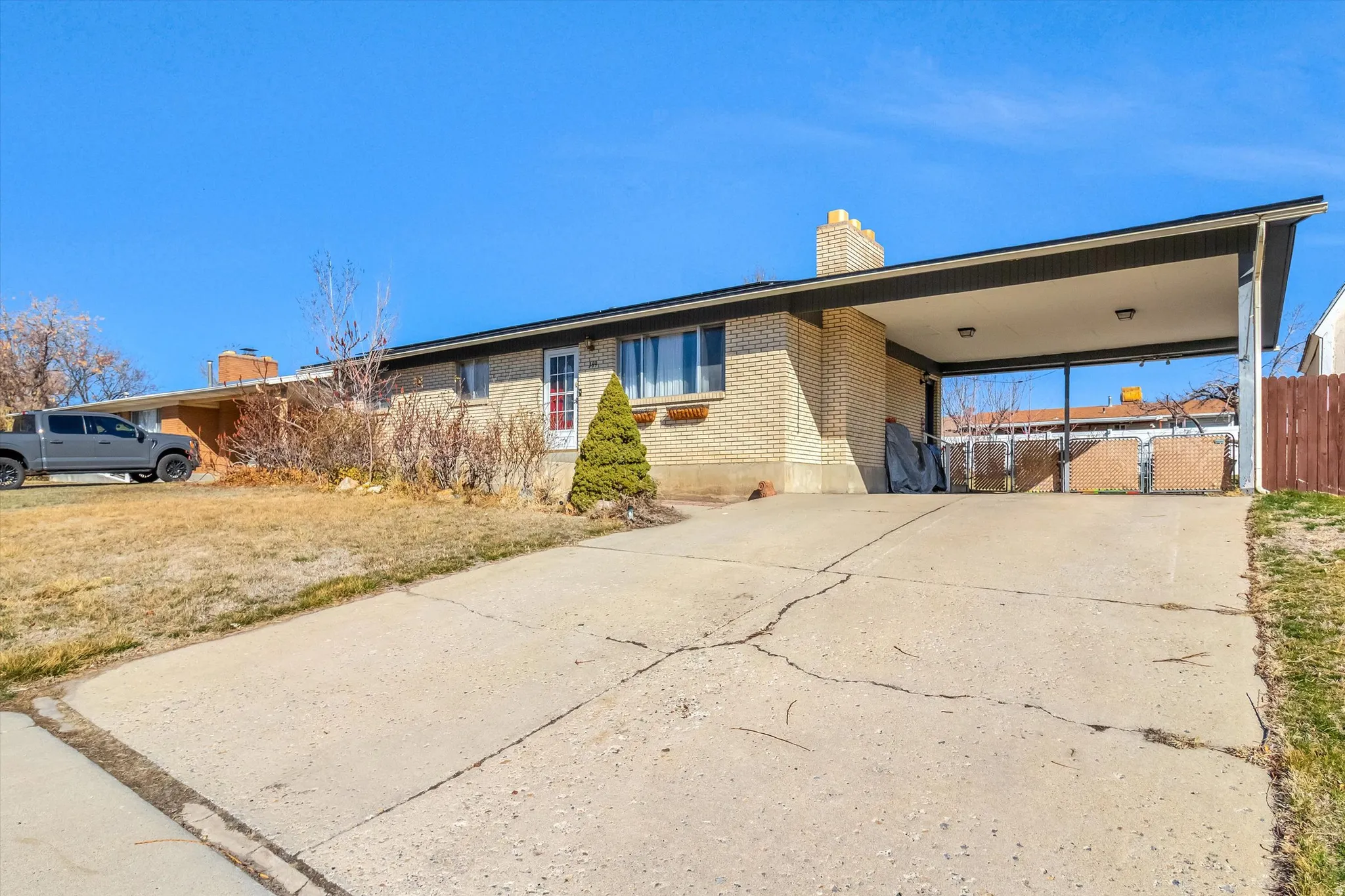 View of front facade featuring a chimney, an attached carport, brick siding, and concrete driveway