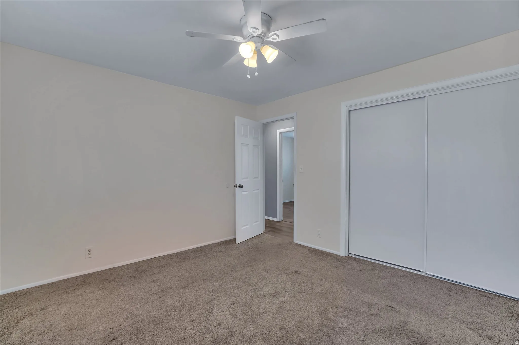 Carpeted room featuring a ceiling fan with integrated lighting, white baseboards, a white interior door, and a white sliding closet door