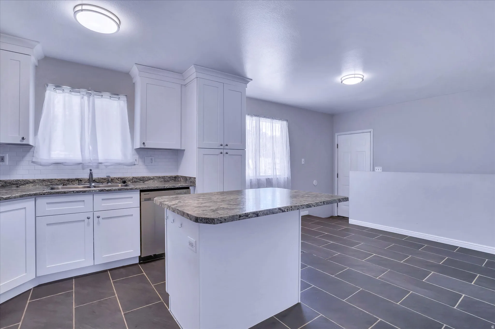 Kitchen featuring white cabinetry, light-colored countertops, subway tile backsplash, stainless-steel dishwasher, and dark rectangular floor tiles