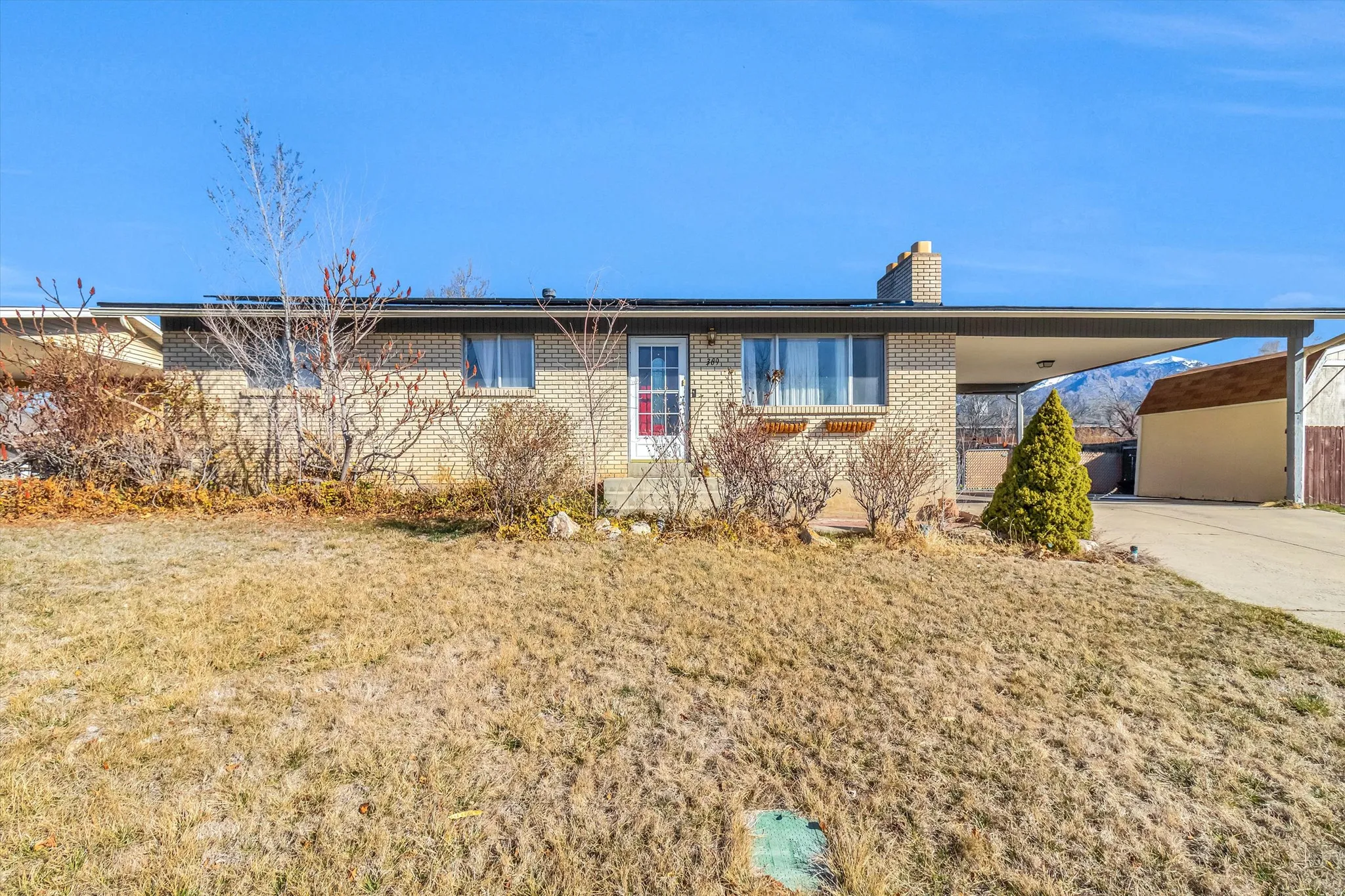 Single story home featuring an attached carport, a front lawn, a chimney, brick siding, and driveway