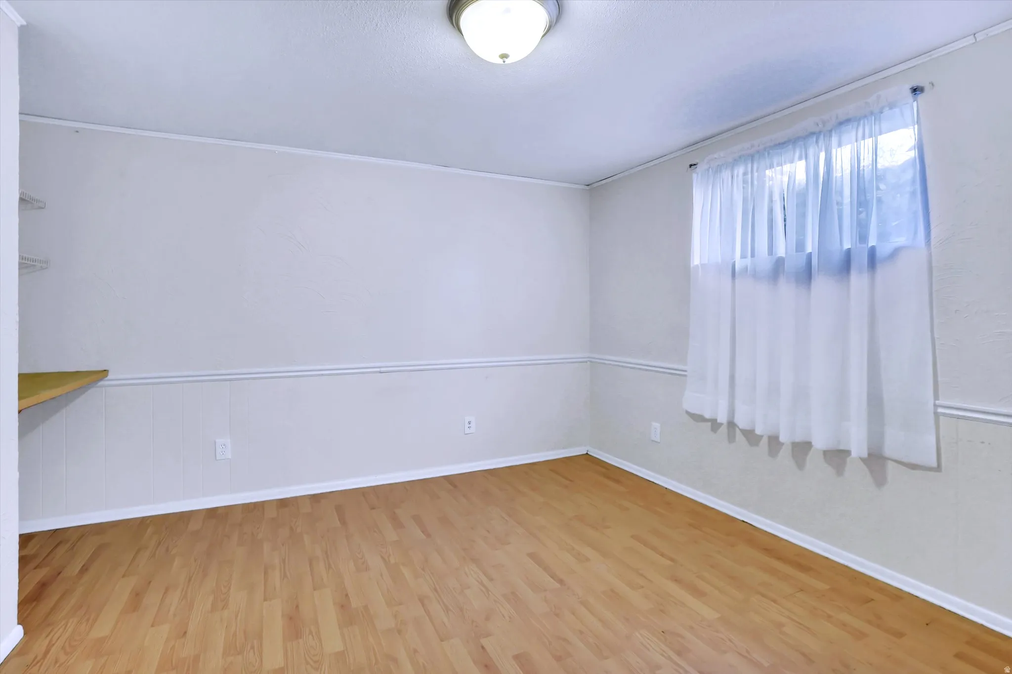 Room featuring wood-finish flooring, white paneled wainscoting, and a white ceiling with a flush-mount light fixture