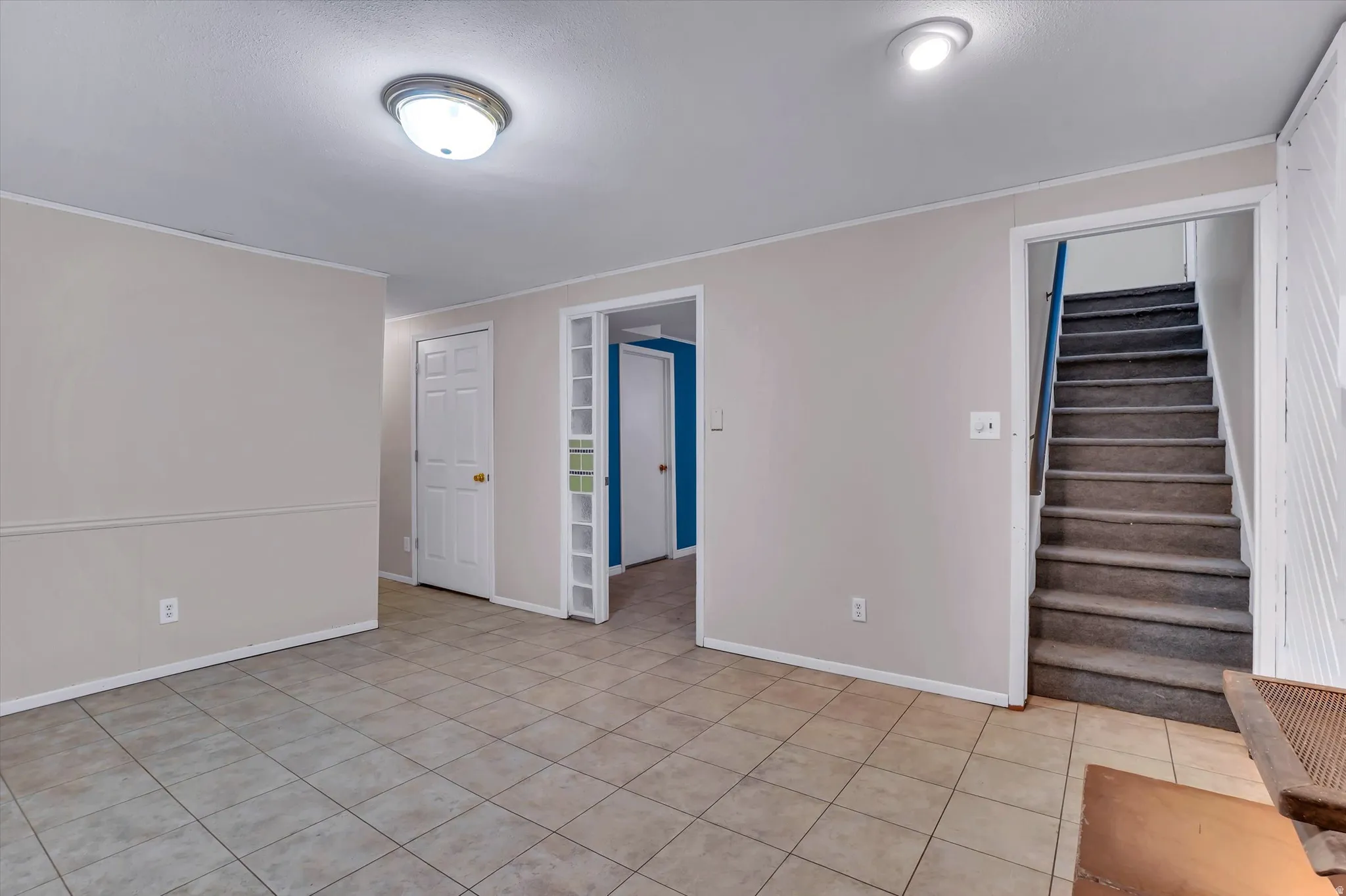 Spacious room featuring neutral tone ceramic tile flooring and light gray walls with wainscoting