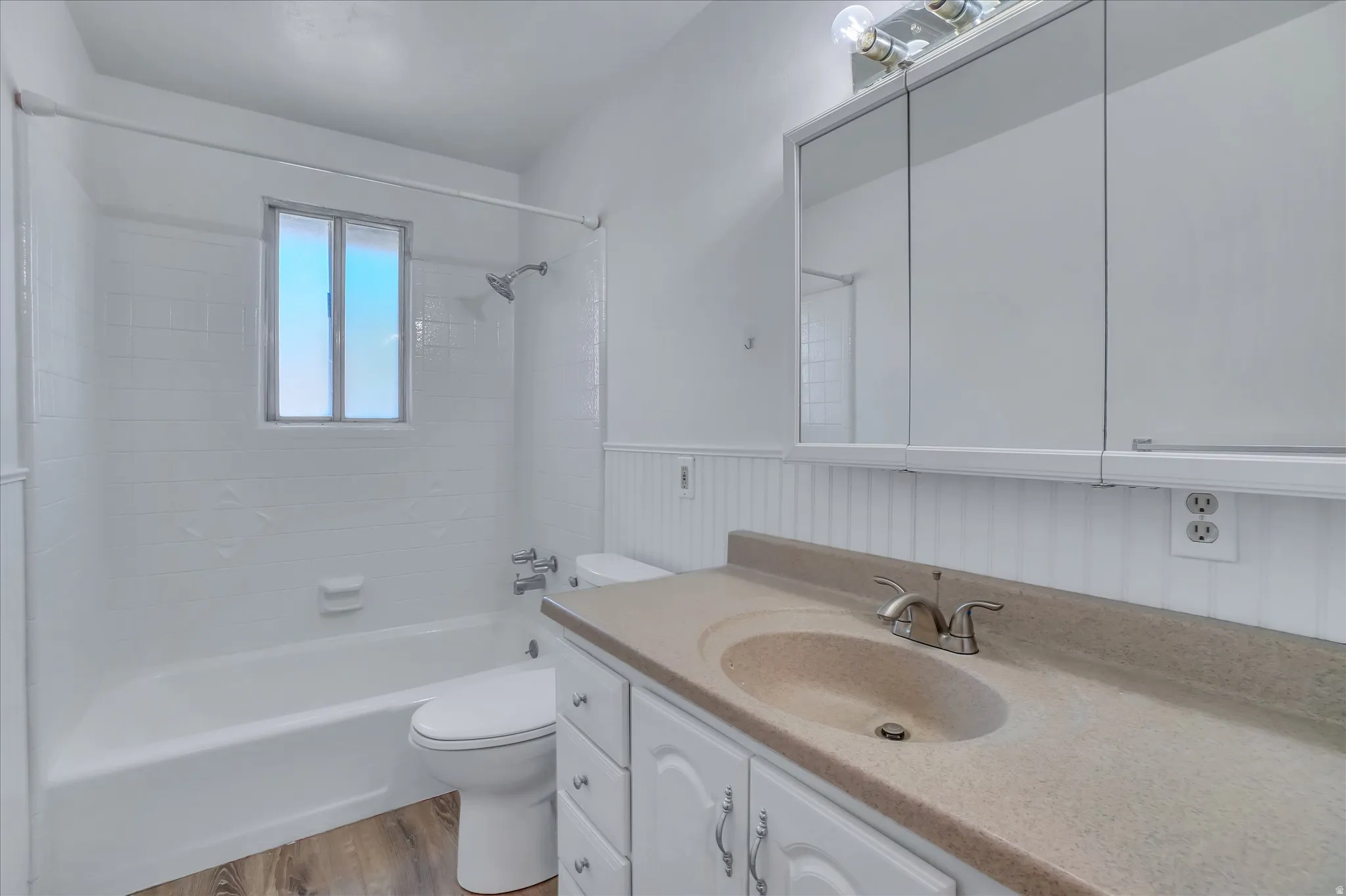 Bathroom featuring a built-in tub with a shower fixture, white tile surround, and a vanity with an integrated sink