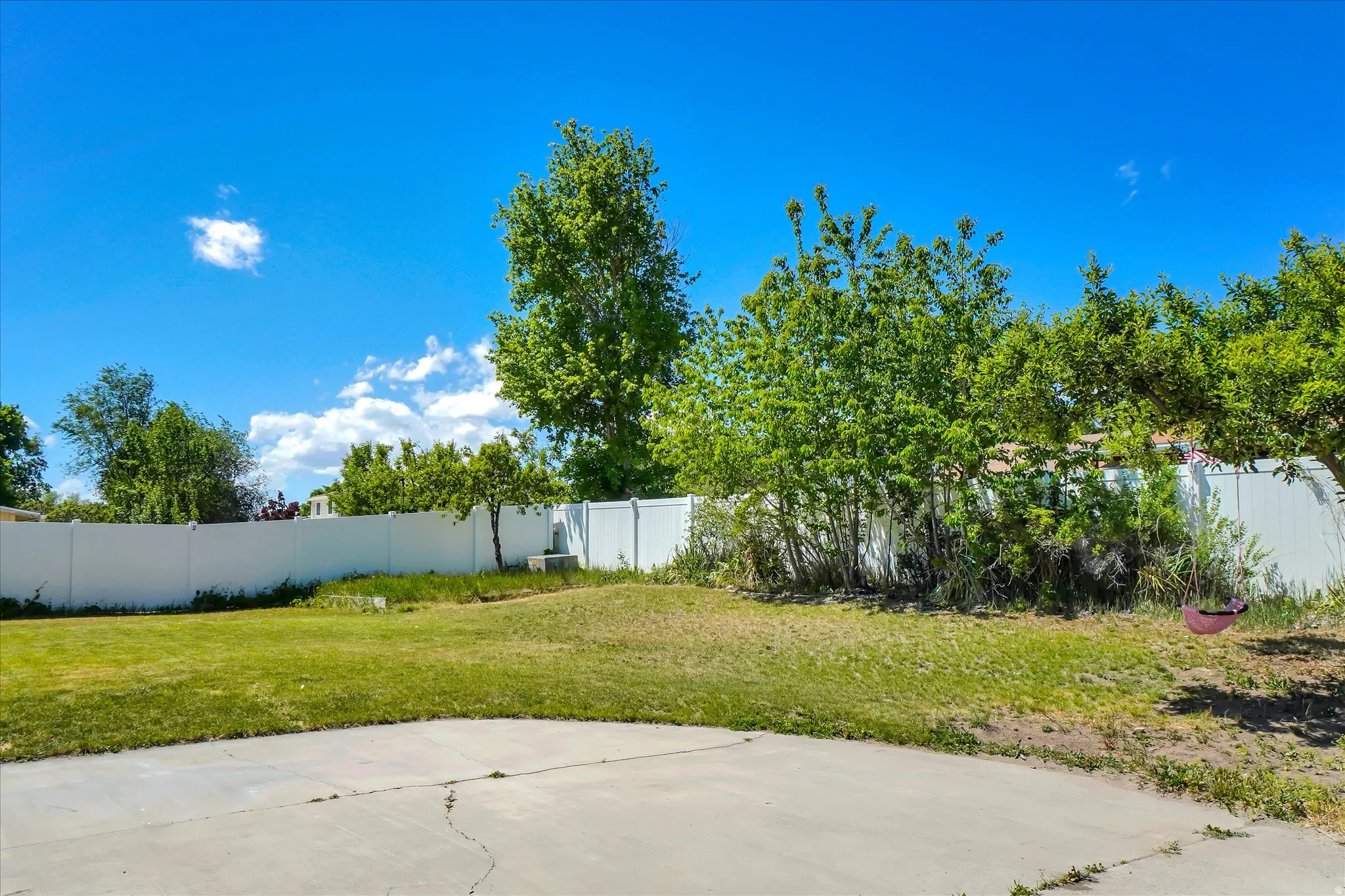 Expansive backyard featuring a concrete patio surface, a broad lawn area, and mature trees
