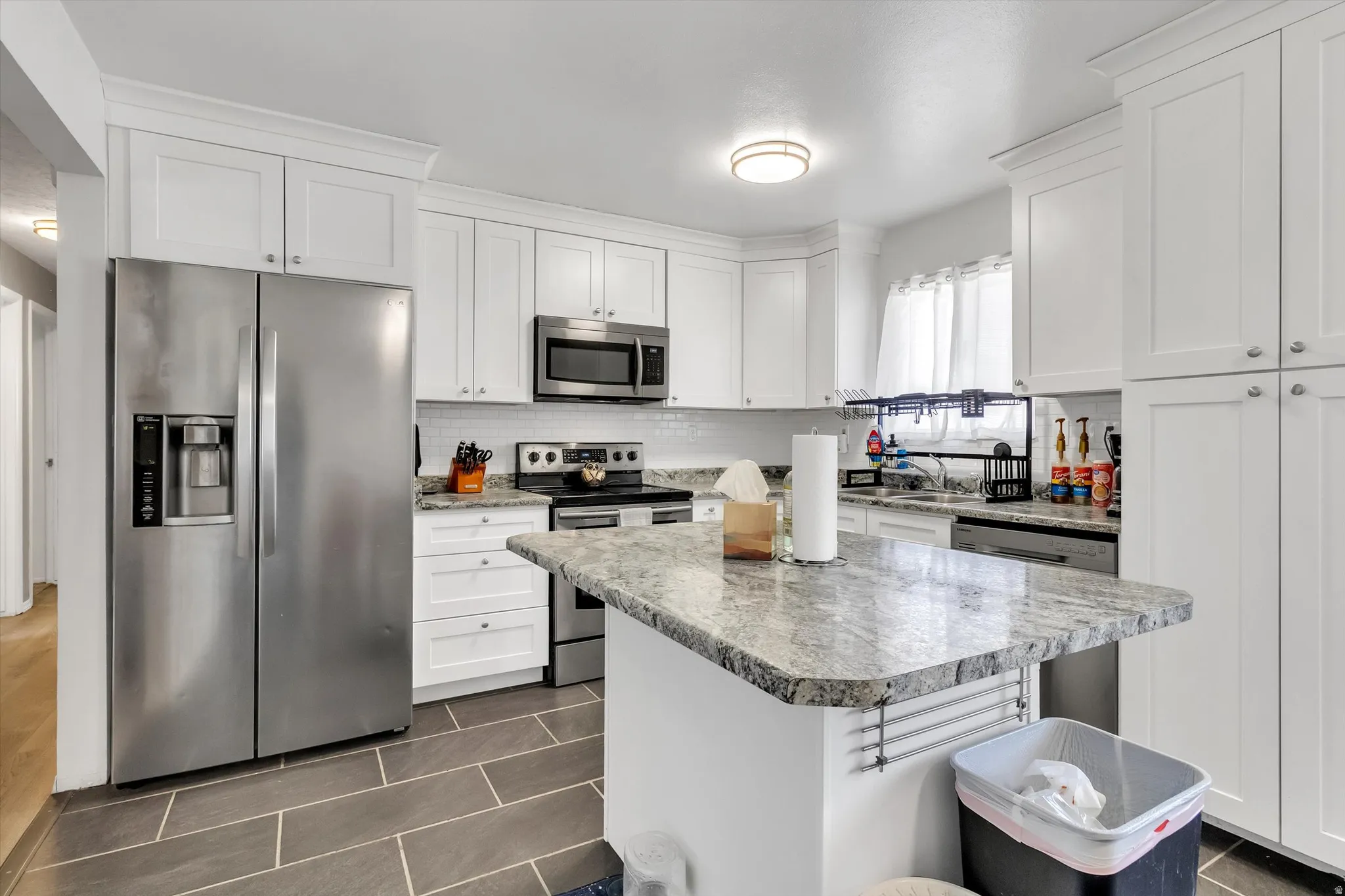 Kitchen with stainless steel appliances, white cabinets, dark tile patterned floors, a kitchen island, and decorative backsplash