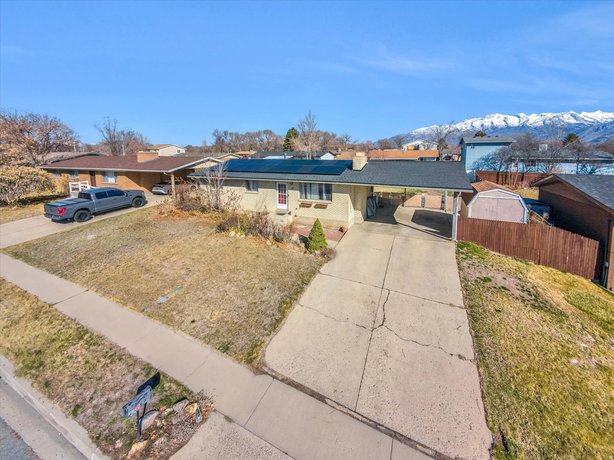 Single story home featuring roof mounted solar panels, a carport, concrete driveway, a mountain view, and brick siding