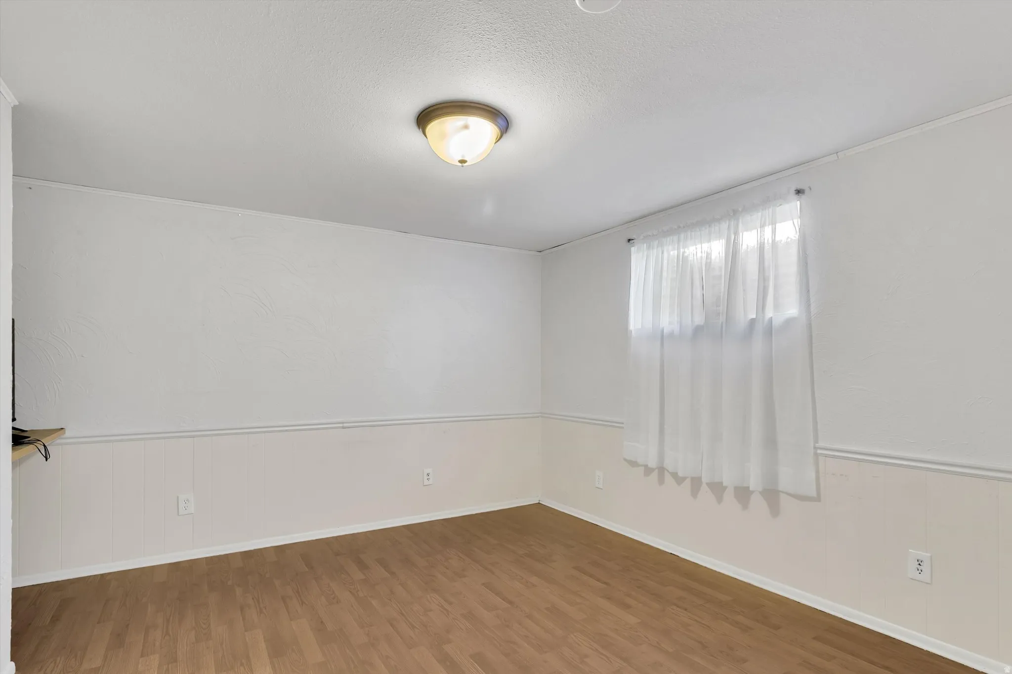 Spare room featuring wainscoting, wood finished floors, a textured ceiling, and wood walls
