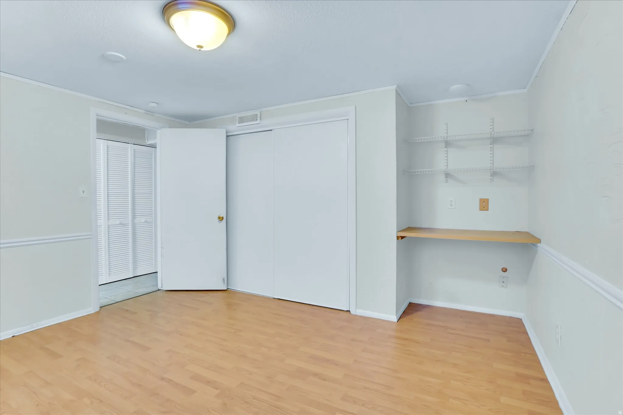 Room featuring wood-finish flooring, white walls with chair rail molding, and a built-in desk with adjustable shelving