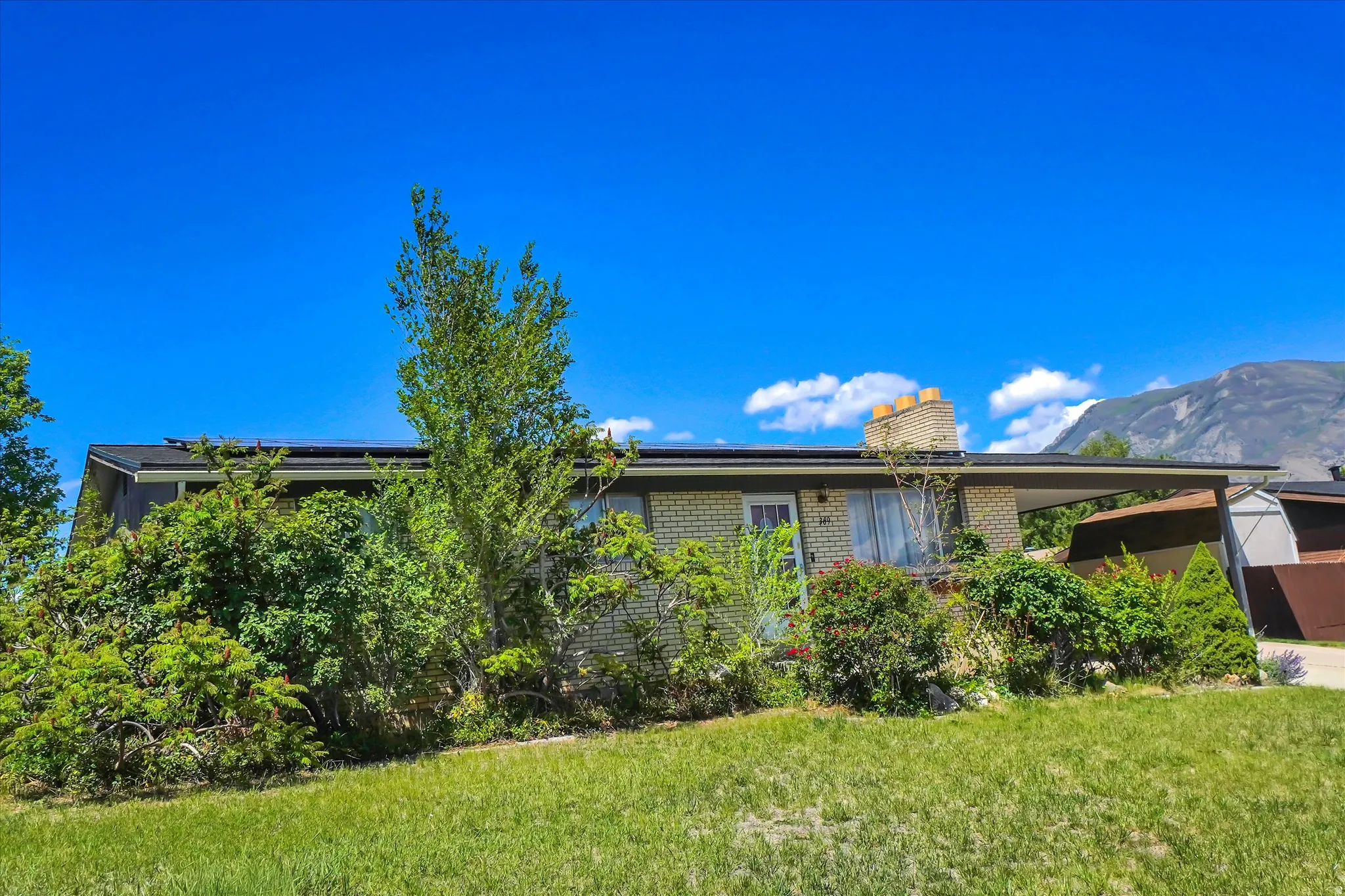 Brick exterior home with a carport, mature landscaping, and an adjacent mountain backdrop