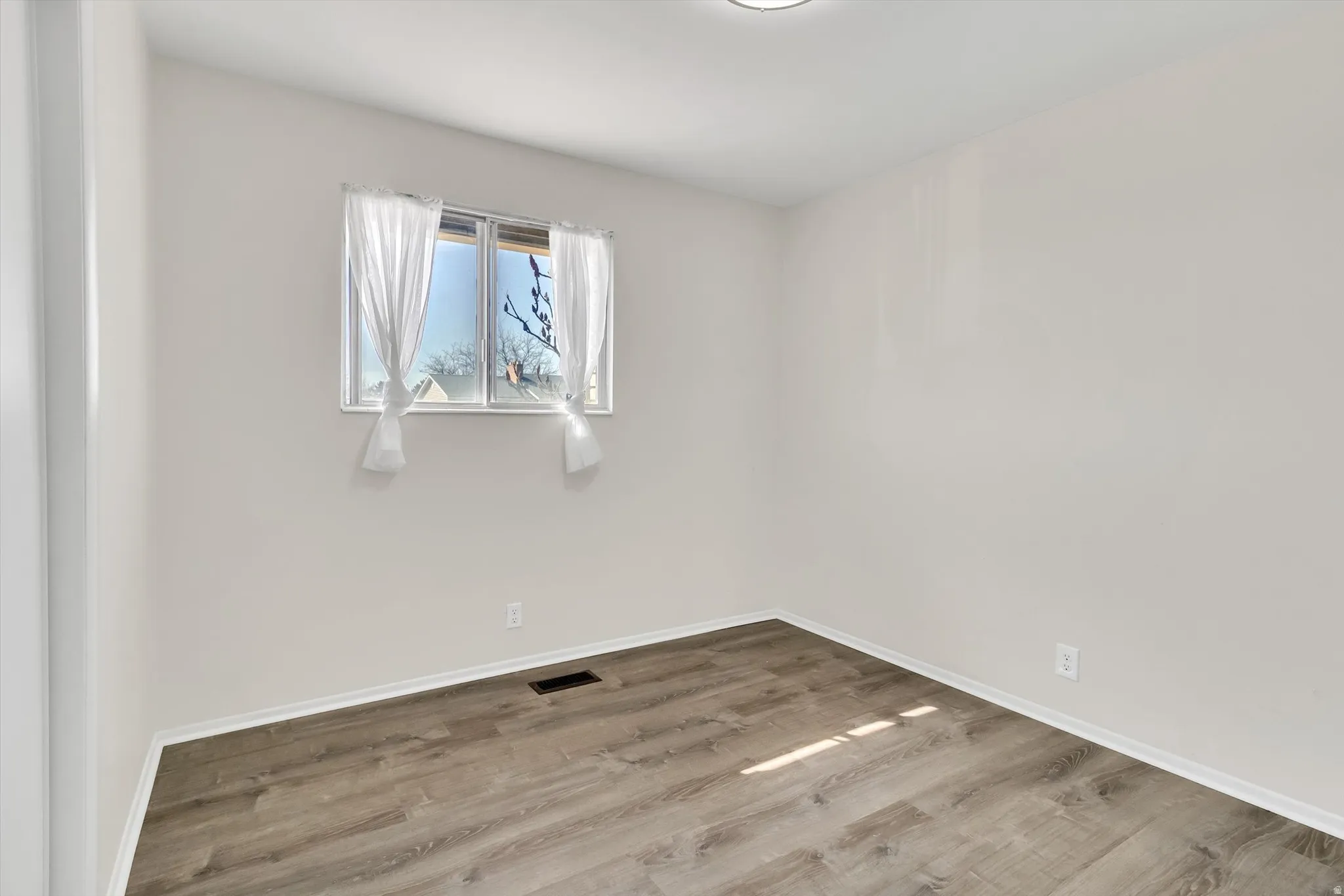 Room with a window, white walls, and wood-finish flooring
