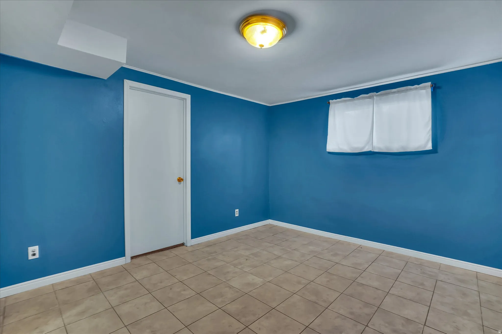 Room featuring blue painted walls, neutral-toned tile flooring, a white interior door, and a flush mount ceiling light fixture