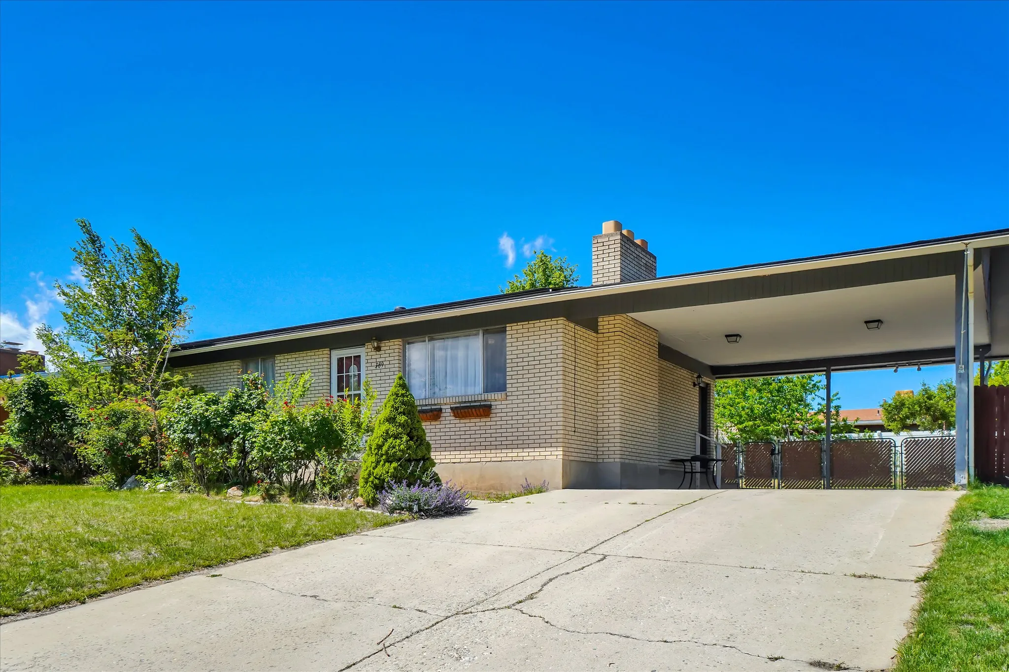 Brick exterior with an attached carport, concrete driveway, and mature landscaping
