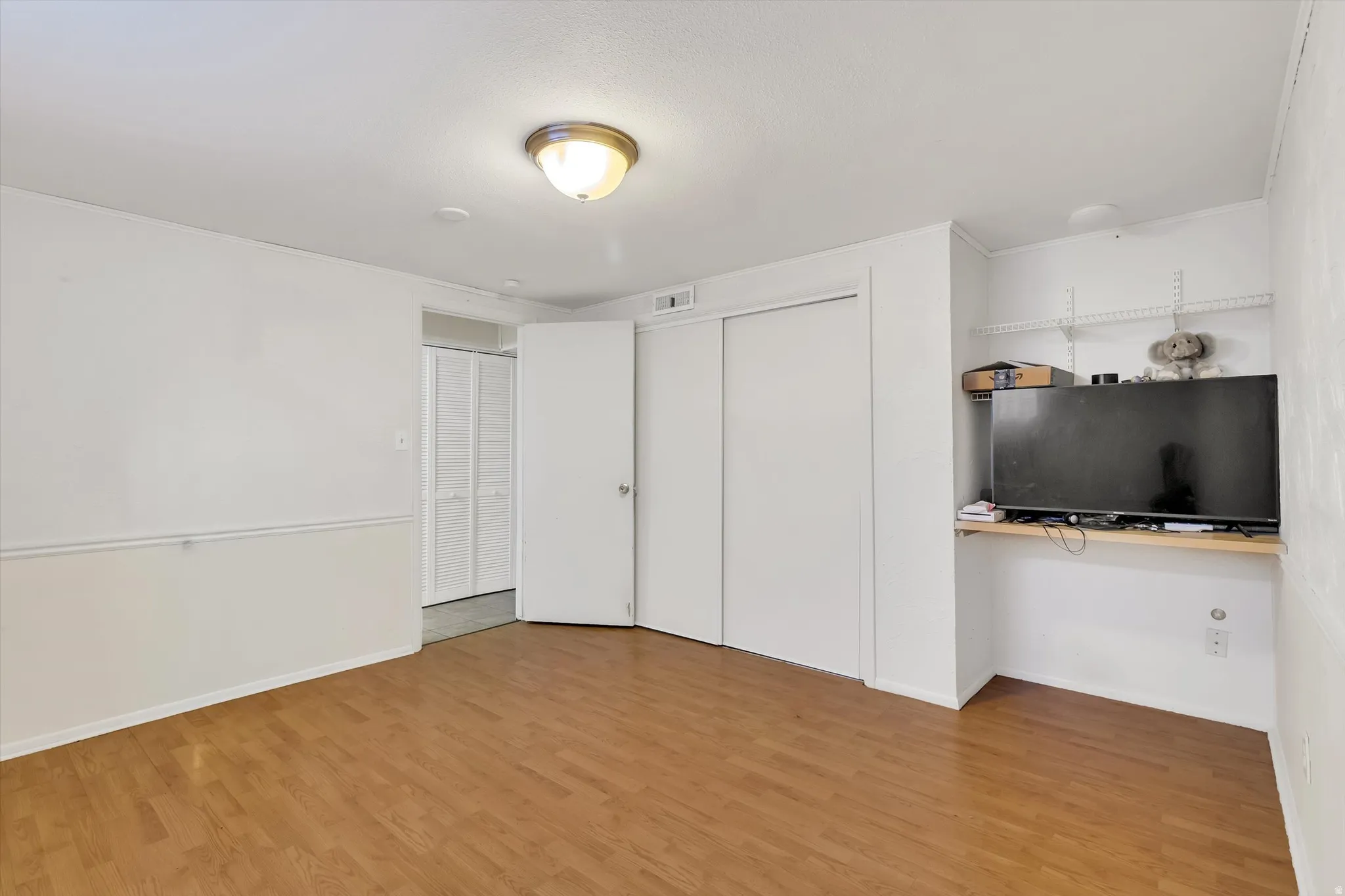 Unfurnished bedroom with light wood-style flooring, a closet, ornamental molding, and built in study area