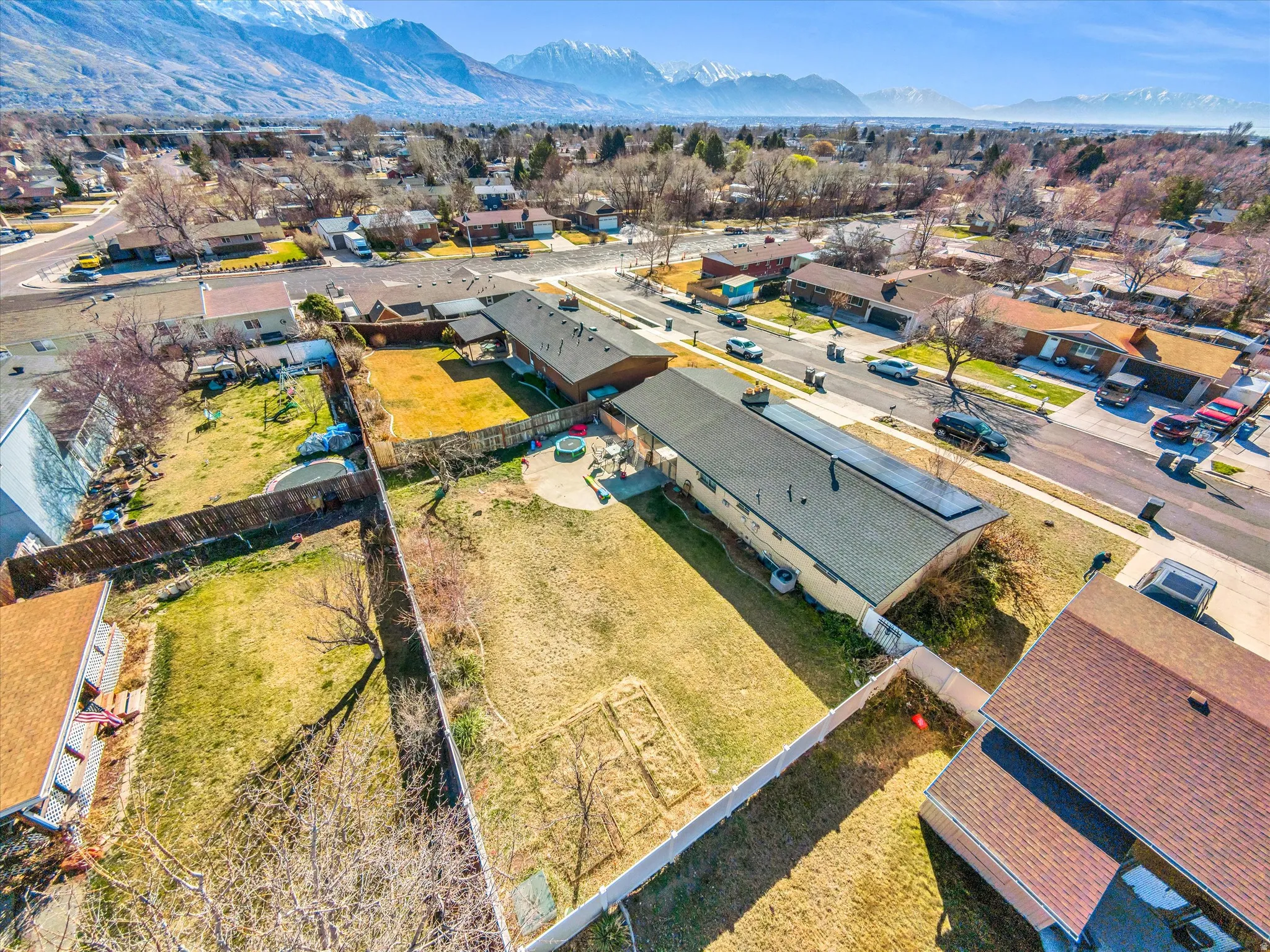 Expansive property featuring a large backyard with fencing, a paved patio, and a shingled roof with solar panels