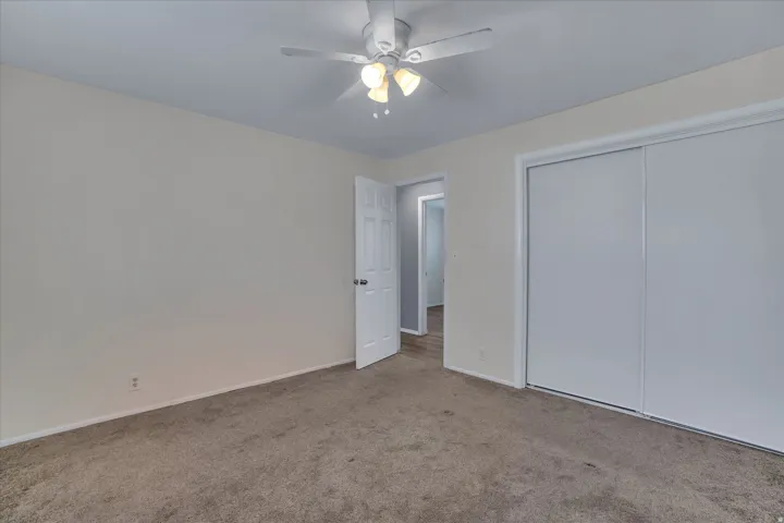 Carpeted room featuring a ceiling fan with integrated lighting, white baseboards, a white interior door, and a white sliding closet door