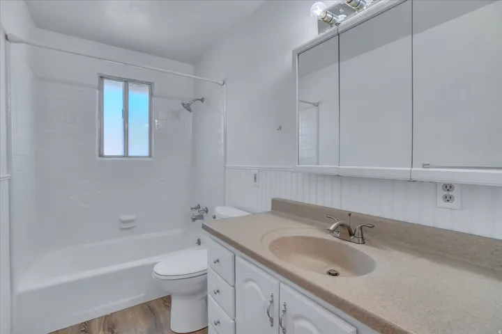 Bathroom featuring a built-in tub with a shower fixture, white tile surround, and a vanity with an integrated sink