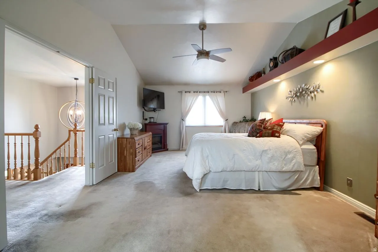 Carpeted bedroom featuring vaulted ceiling, suspended lighting, and ceiling fan