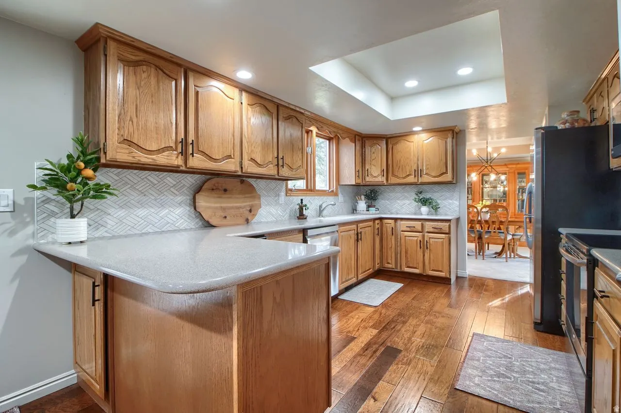 Kitchen featuring wood finish cabinets, recessed lighting, dark wood finished floors, a peninsula, and a tray ceiling